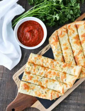 These easy Cheesy Garlic Breadsticks are loaded with garlic, cheese, and herbs for a great tasting breadstick to enjoy for pizza night. Also delicious dipped in marinara sauce!