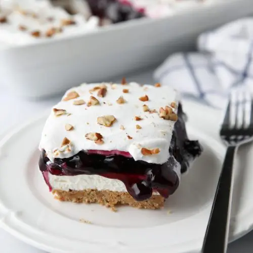 Blueberry Delight (aka Blueberry Lush) is an easy layered dessert with a graham cracker and pecan crust, no bake cheesecake, blueberry pie filling, and cool whip topping. A light, fruity, and delicious summer dessert with minimal baking.