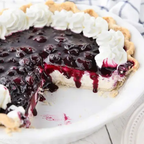 Blueberry Cream Cheese Pie with whipped cream on top and a couple slices missing from dish.