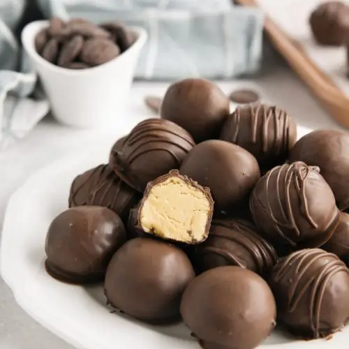 Easy peanut butter balls stacked on a plate focusing in on one that has been cut in half to show the inside.