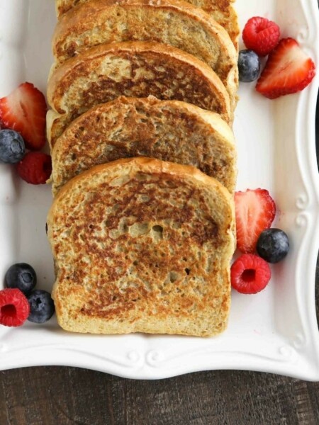 Plate of cinnamon french toast with fruit and syrup on the side.