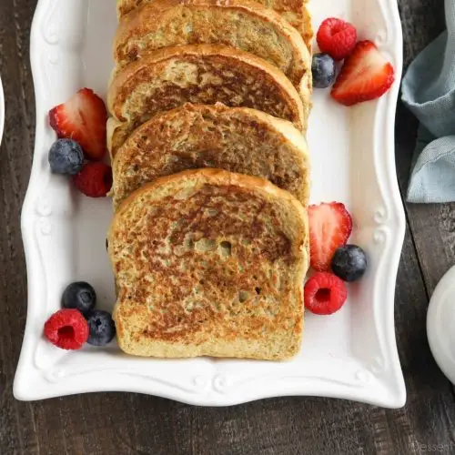 Plate of cinnamon french toast with fruit and syrup on the side.