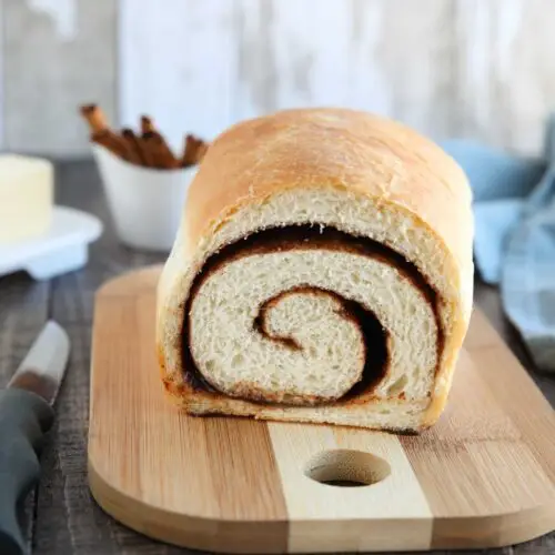 Loaf of cinnamon bread on a cutting board with a slice removed to show the cinnamon swirl on the inside..