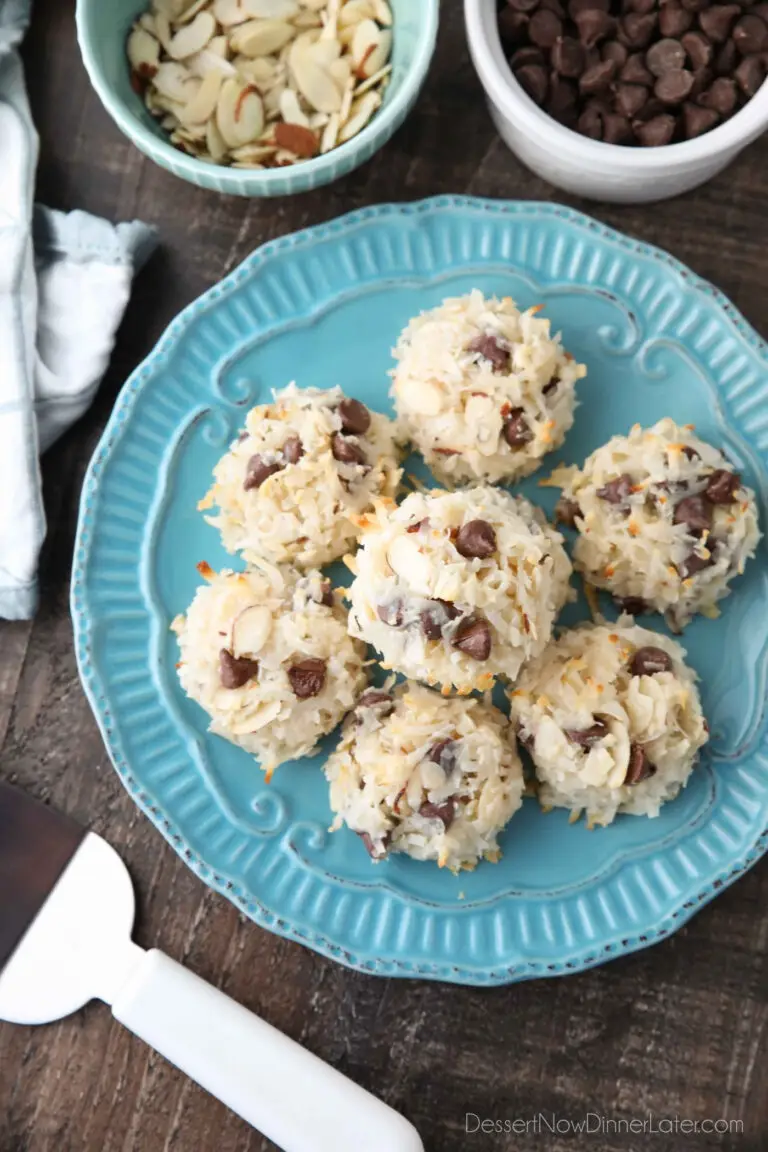 Top view of Almond Joy Cookies (chocolate almond macaroons) on a plate with bowls of chocolate chips and sliced almonds on the side.