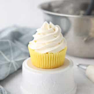 Focus is on a cupcake piled high with whipped cream cheese frosting.