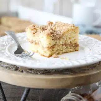 Close up of a slice of sour cream coffee cake on a plate with a line of cinnamon streusel in the center of the cake and more streusel on top.