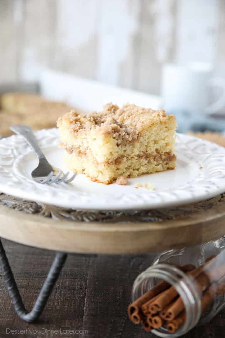 Close up of a slice of sour cream coffee cake on a plate with a line of cinnamon streusel in the center of the cake and more streusel on top.