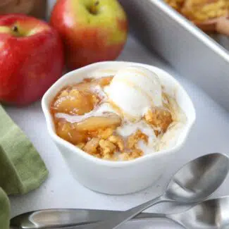 Close up of a bowl full of caramel apple dump cake and vanilla ice cream on top.