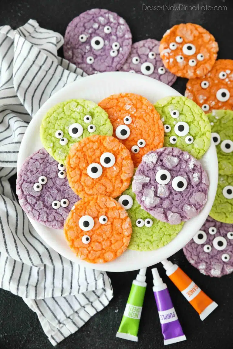 Bright colored Halloween cookies on a plate with powdered sugar cracks and candy eyeballs.