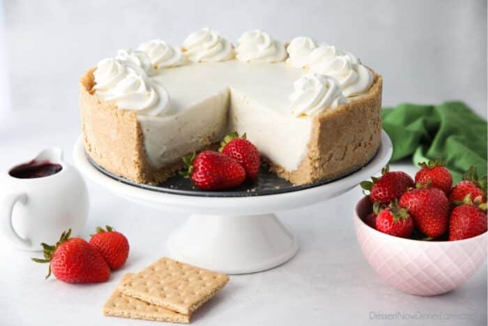 No bake cheesecake on a cake plate with a couple slices taken out and fresh strawberries on the side.