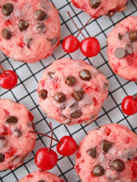 Close up top view of cherry chocolate chip cookies on a wire cooling rack with maraschino cherries on the side.