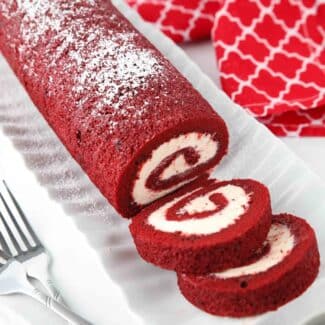 Red Velvet Cake Roll on a platter with a couple of slices cut.