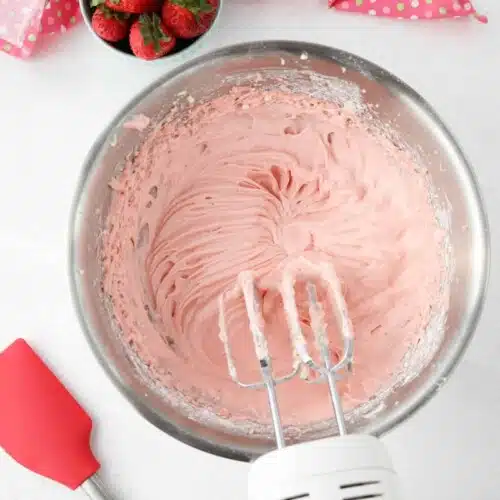 Strawberry cream cheese frosting in bowl with electric mixer and beaters.