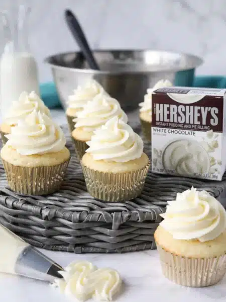 Cupcakes topped with white chocolate pudding buttercream frosting made with instant pudding mix.