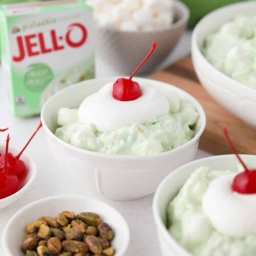 Close up of pistachio fluff in a bowl with whipped cream and a cherry on top.