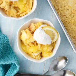 Lemon Dump Cake in a small bowl topped with whipped topping and a lemon slice.
