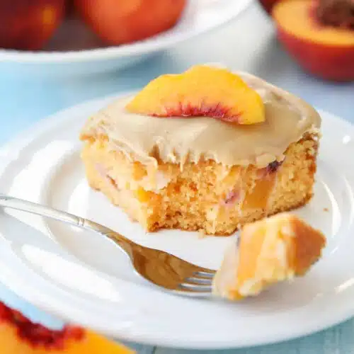 Fork full of peach cake with brown sugar frosting taken out of a slice on a plate.