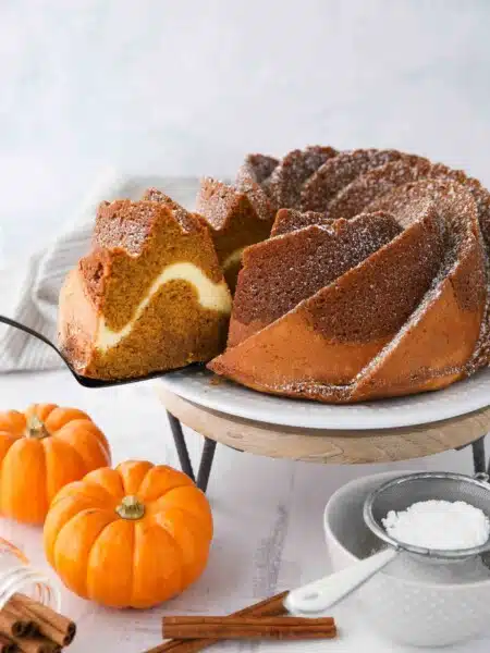 Slice of pumpkin bundt cake with cream cheese filling being served with a spatula.