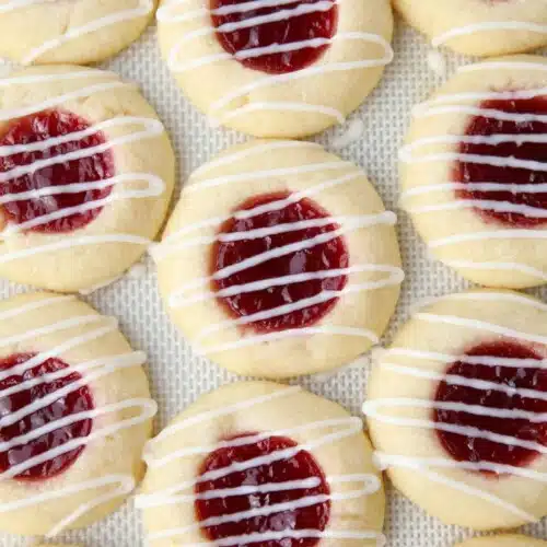 Icing drizzled on top of raspberry thumbprint cookies on a silicone baking mat.