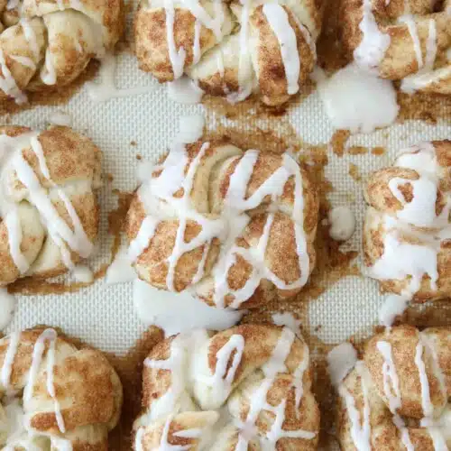 Icing drizzled over baked cinnamon roll knots.