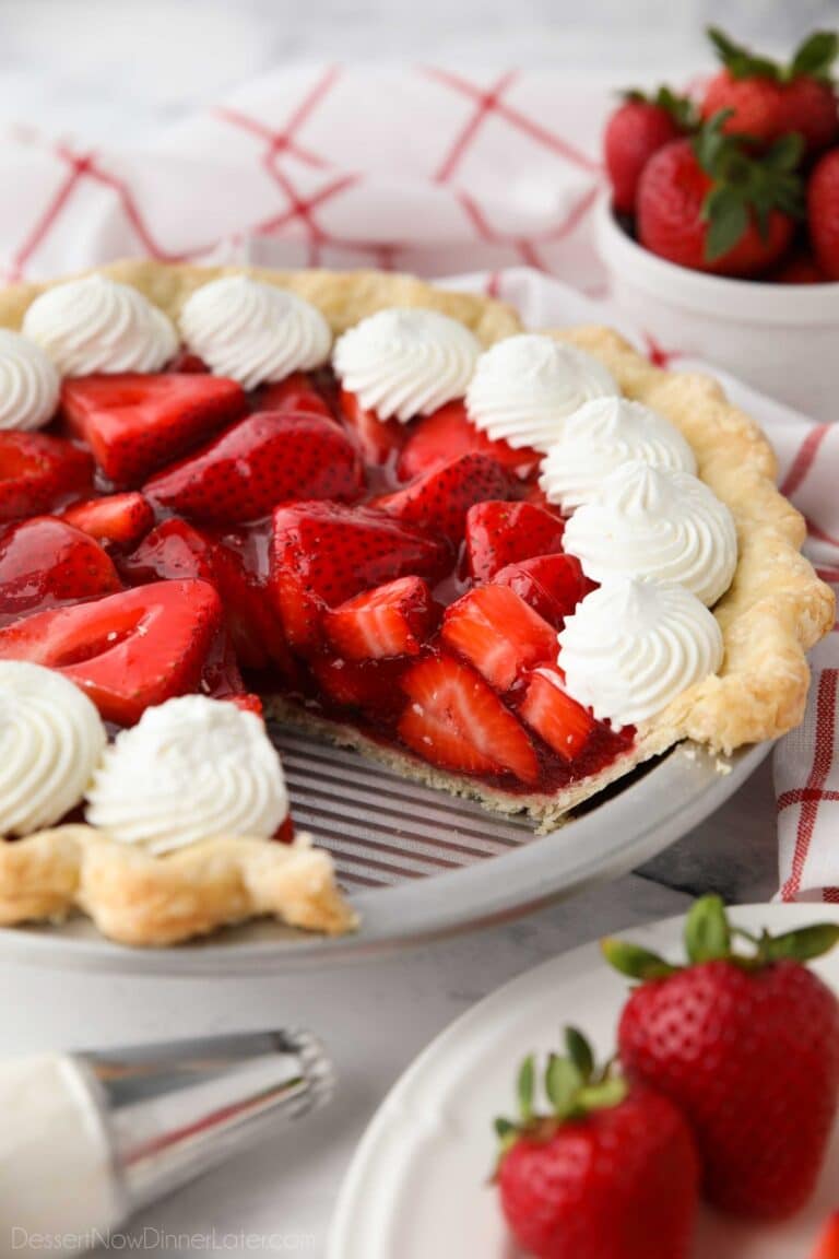 Fresh strawberry pie topped with whipped cream with a slice taken out of the pan.