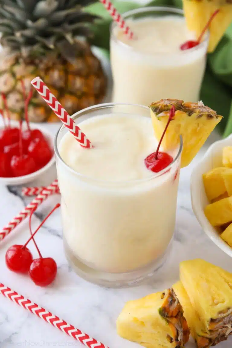 Virgin pina colada in a glass cup with a wedge of pineapple, a maraschino cherry, and a straw.