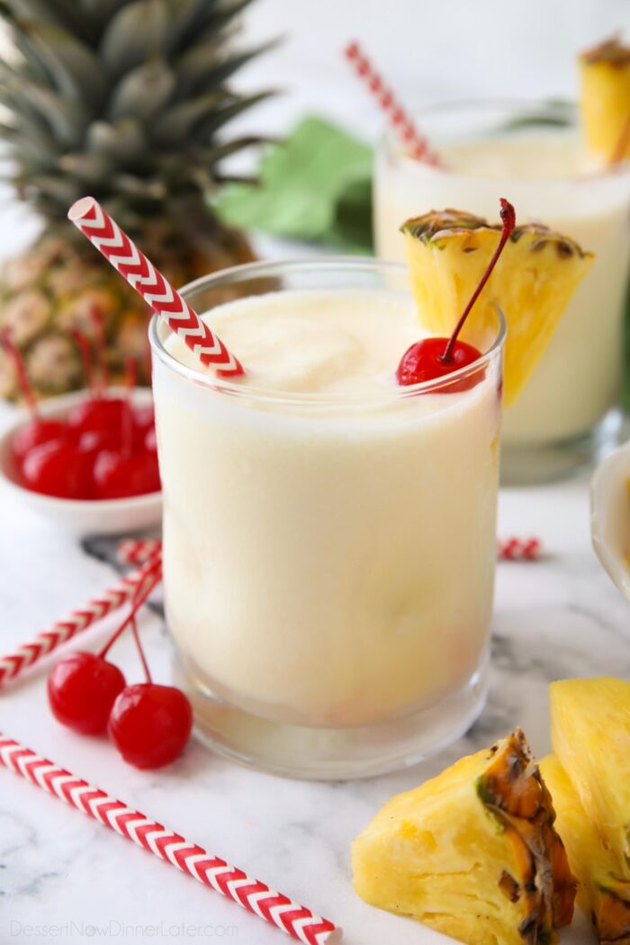 Non alcoholic pina colada mocktail in a glass cup with a wedge of pineapple, a maraschino cherry, and a straw.