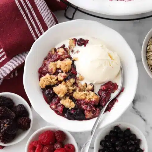 Bowl full of warm berry crisp with ice cream on top.