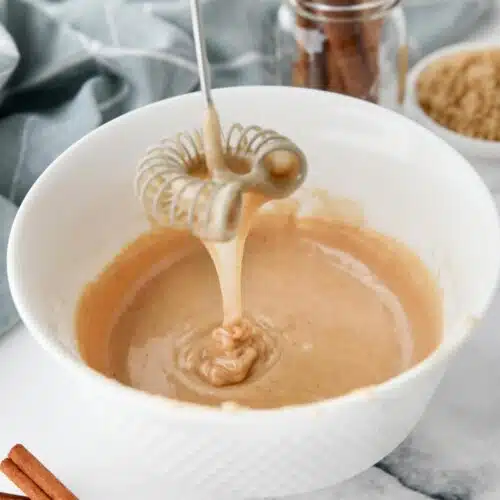 Cinnamon brown sugar glaze dripping off of a whisk into a bowl.