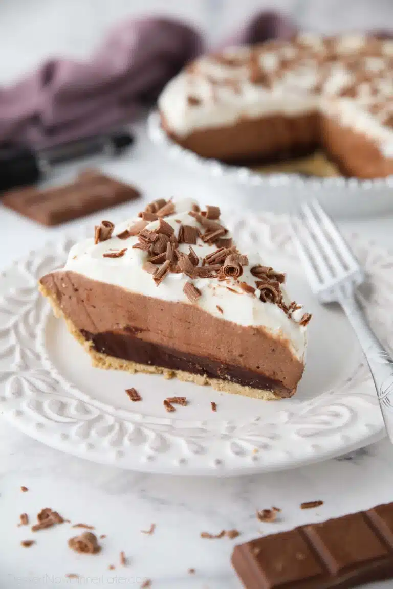 Slice of chocolate truffle pie on a plate showing a graham cracker crust and layers of ganache, whipped chocolate, whipped cream, and chocolate shavings on top.