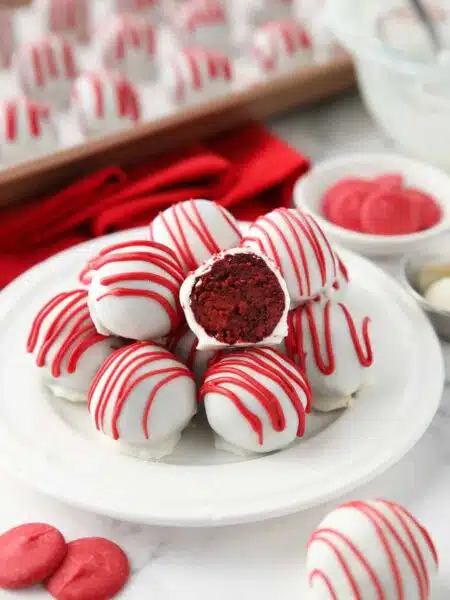 Red Velvet Truffles on a plate with one cut open showing the red cake inside of the white chocolate shell.