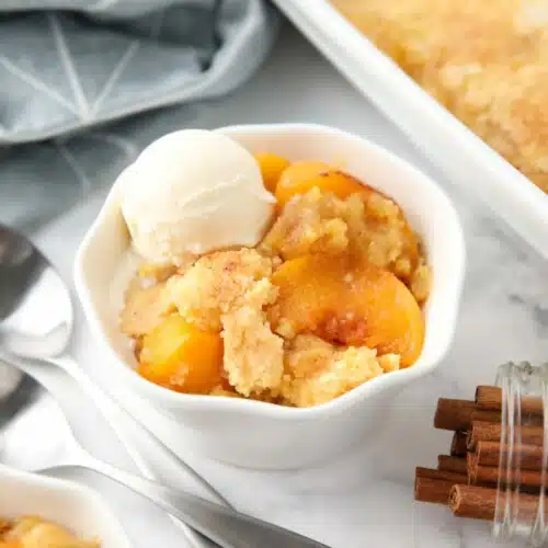 Peach dump cake (aka peach cobbler with cake mix) in a bowl with a scoop of vanilla ice cream.