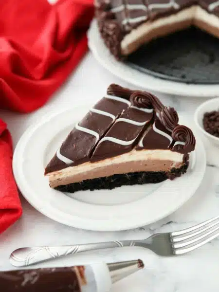 Slice of Olive Garden Black Tie Mousse Cake on a plate showing layers of chocolate cake, chocolate mousse, vanilla mousse, with swirled white and dark chocolate ganache on top.