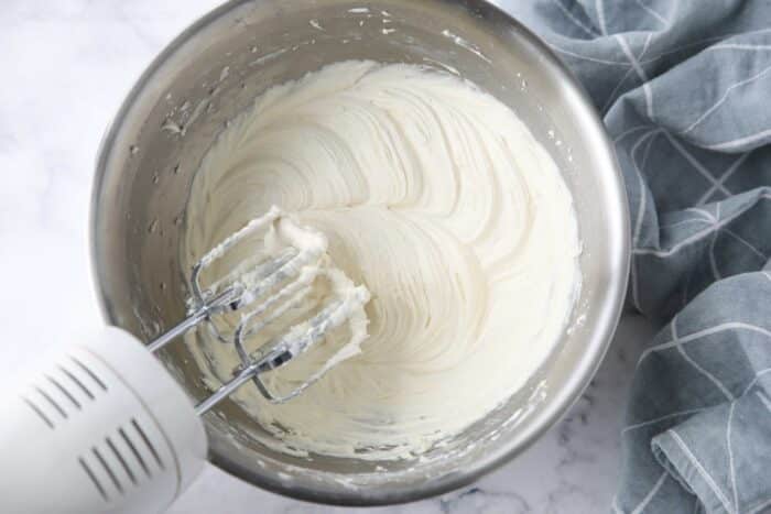 Cream cheese frosting made in a bowl with an electric hand mixer.