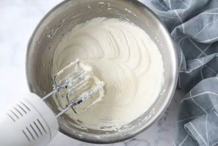 Cream cheese frosting made in a bowl with an electric hand mixer.