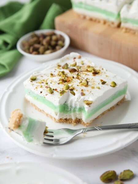 Layered pistachio dessert on a plate with a fork-full taken out.