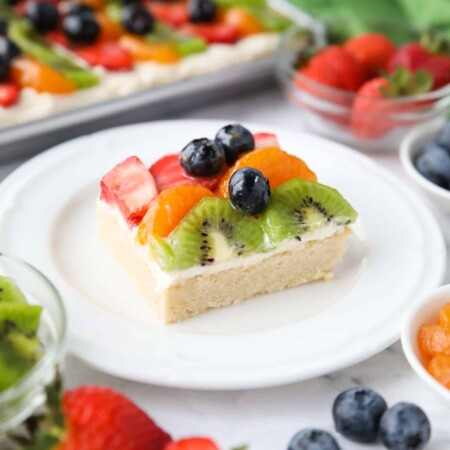 Square of sugar cookie fruit pizza on a plate.