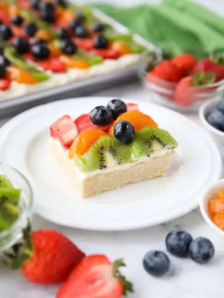 Square of sugar cookie fruit pizza on a plate.