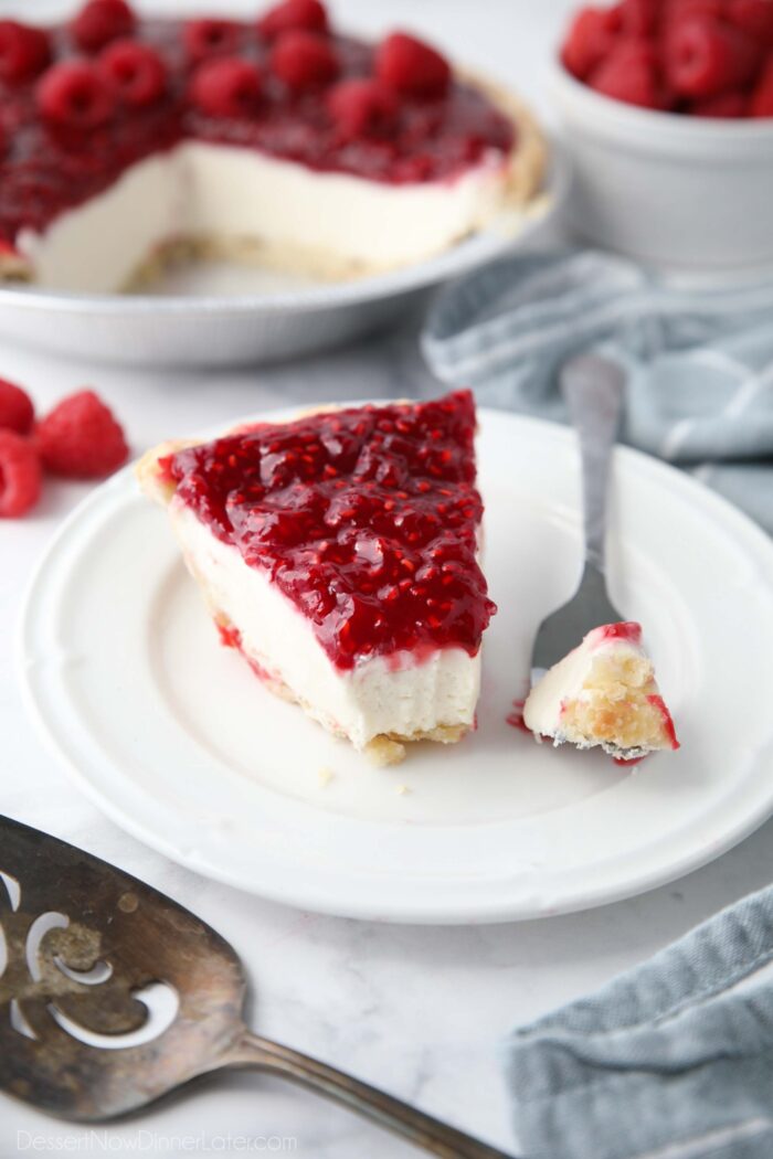 Slice of Raspberry Cream Pie on a plate with a forkful taken out to show layers of pastry crust, whipped cream cheese filling, and raspberry topping.