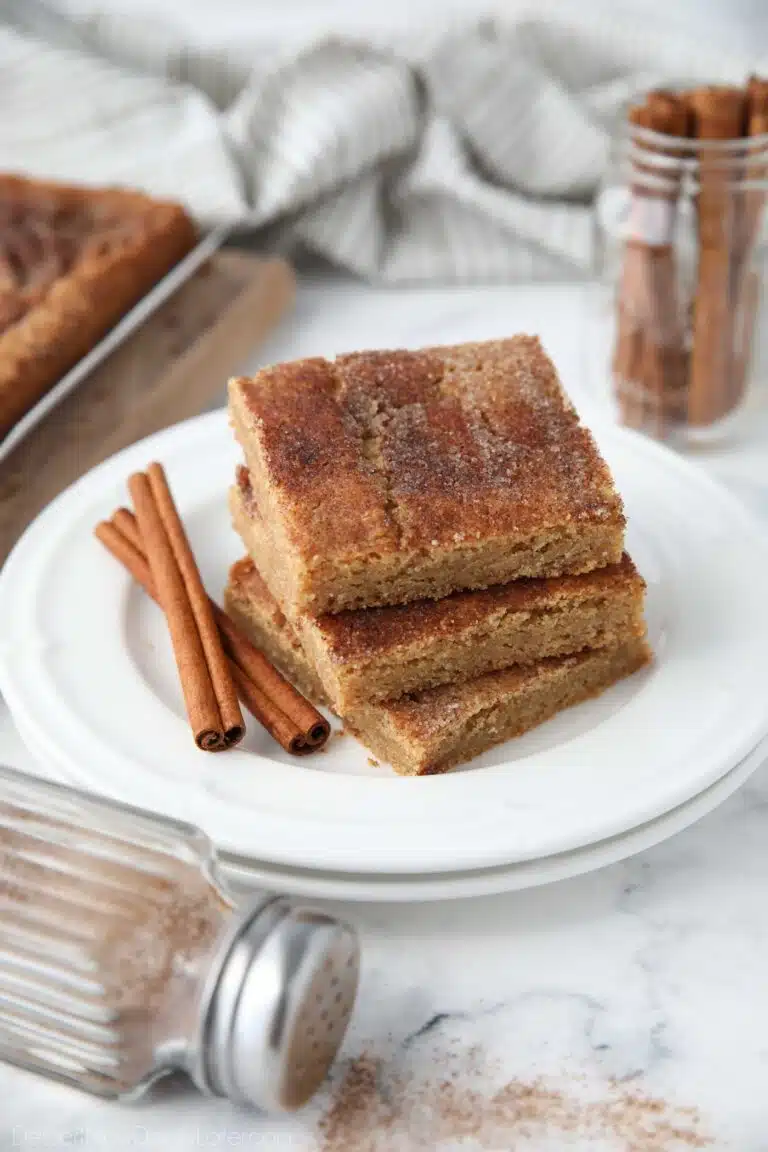 Stack of cinnamon bars on a plate with extra cinnamon-sugar on top and cinnamon sticks on the side.