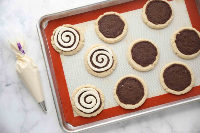 Piping frosting into a swirl on top of cinnamon roll sugar cookies.