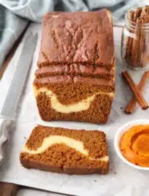 A loaf of pumpkin cream cheese bread with a few slices cut, showing a swirl of cream cheese in the center.