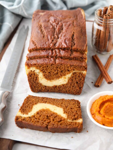 A loaf of pumpkin cream cheese bread with a few slices cut, showing a swirl of cream cheese in the center.