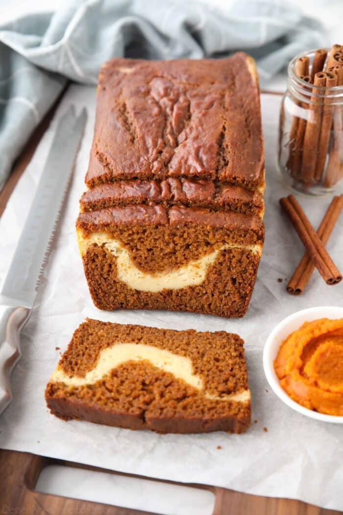 A loaf of pumpkin cream cheese bread with a few slices cut, showing a swirl of cream cheese in the center.