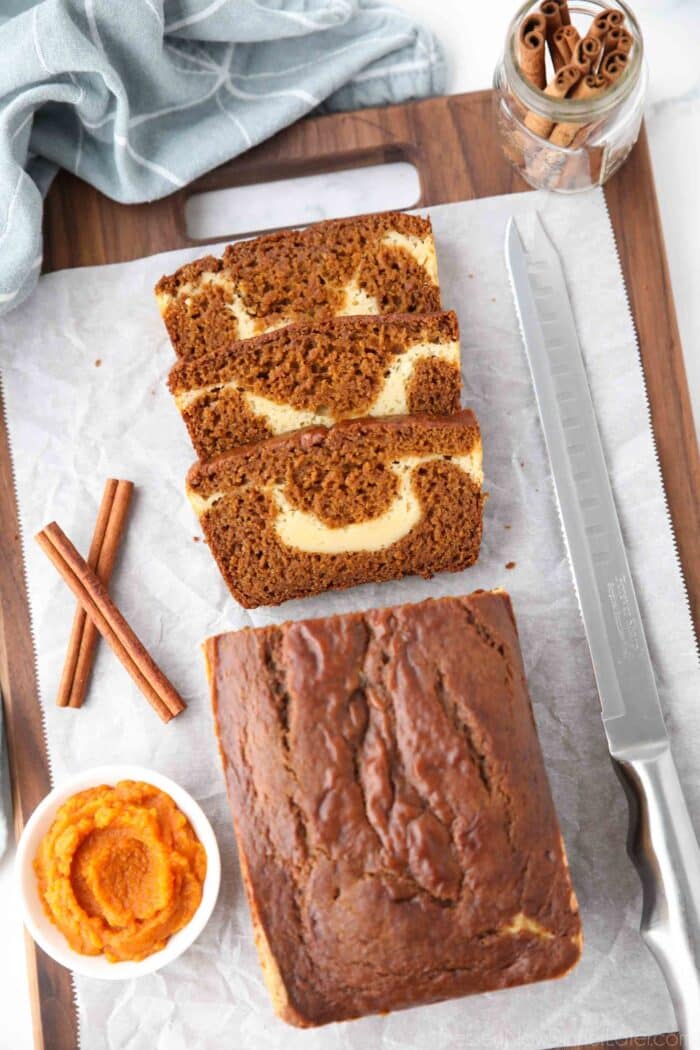 A loaf of pumpkin bread with a few slices cut, showing a ribbon of cream cheese in the center.