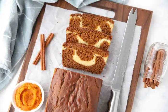 A loaf of pumpkin cream cheese bread with a few slices cut, showing a swirl of cream cheese in the center.