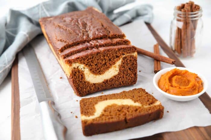 A loaf of pumpkin bread with a few slices cut, showing a ribbon of cream cheese in the center.