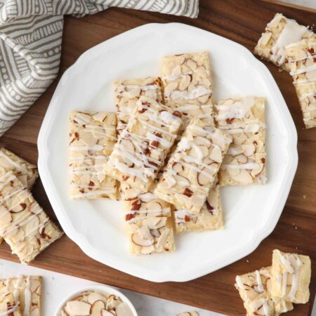 Thin rectangle almond bars with sliced almonds and drizzled glaze on a plate.