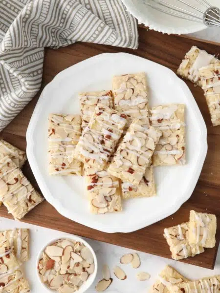 Thin rectangle almond bars with sliced almonds and drizzled glaze on a plate.