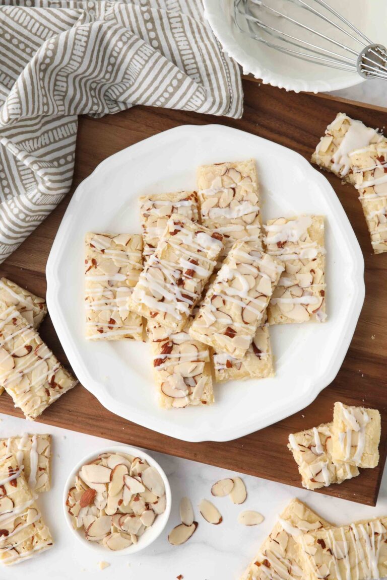 Thin rectangle almond bars with sliced almonds and drizzled glaze on a plate.